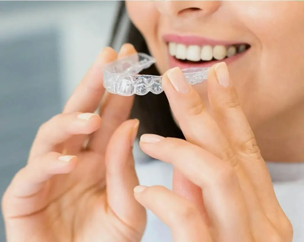An adult holding a teeth retainer near their mouth, smiling and preparing to place it over their upper teeth.