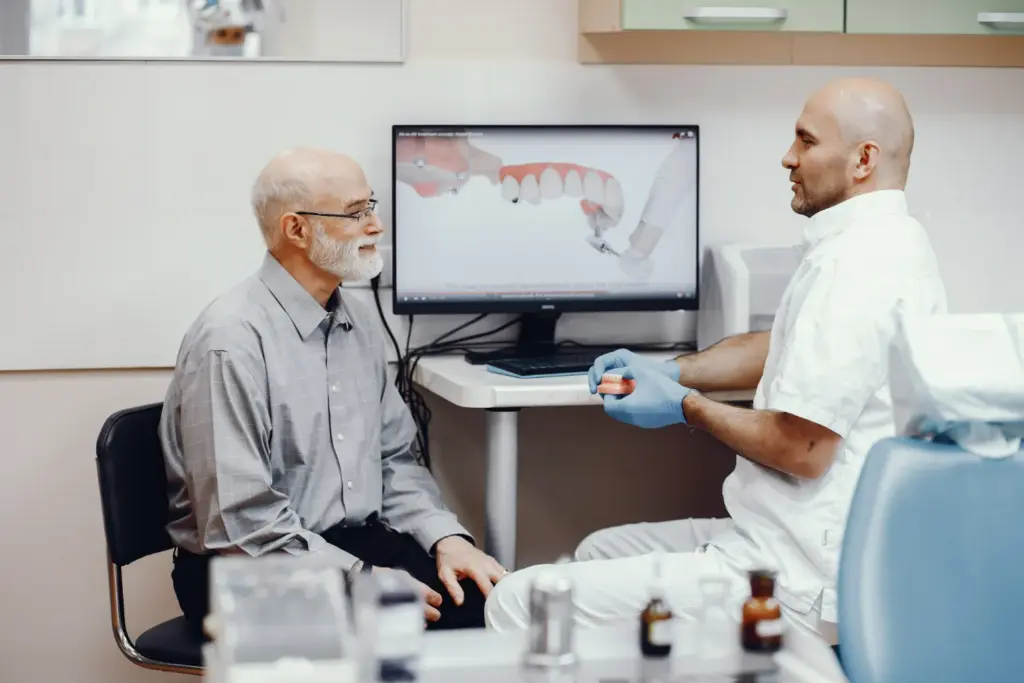 Patient consulting with a dentist about types of dental implants using a 3D model and treatment plan on screen.