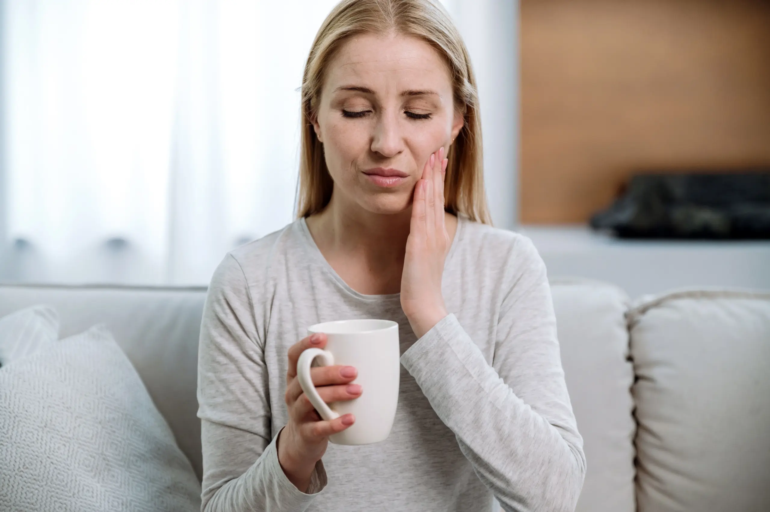 Woman feeling tooth pain drinking hot drink.