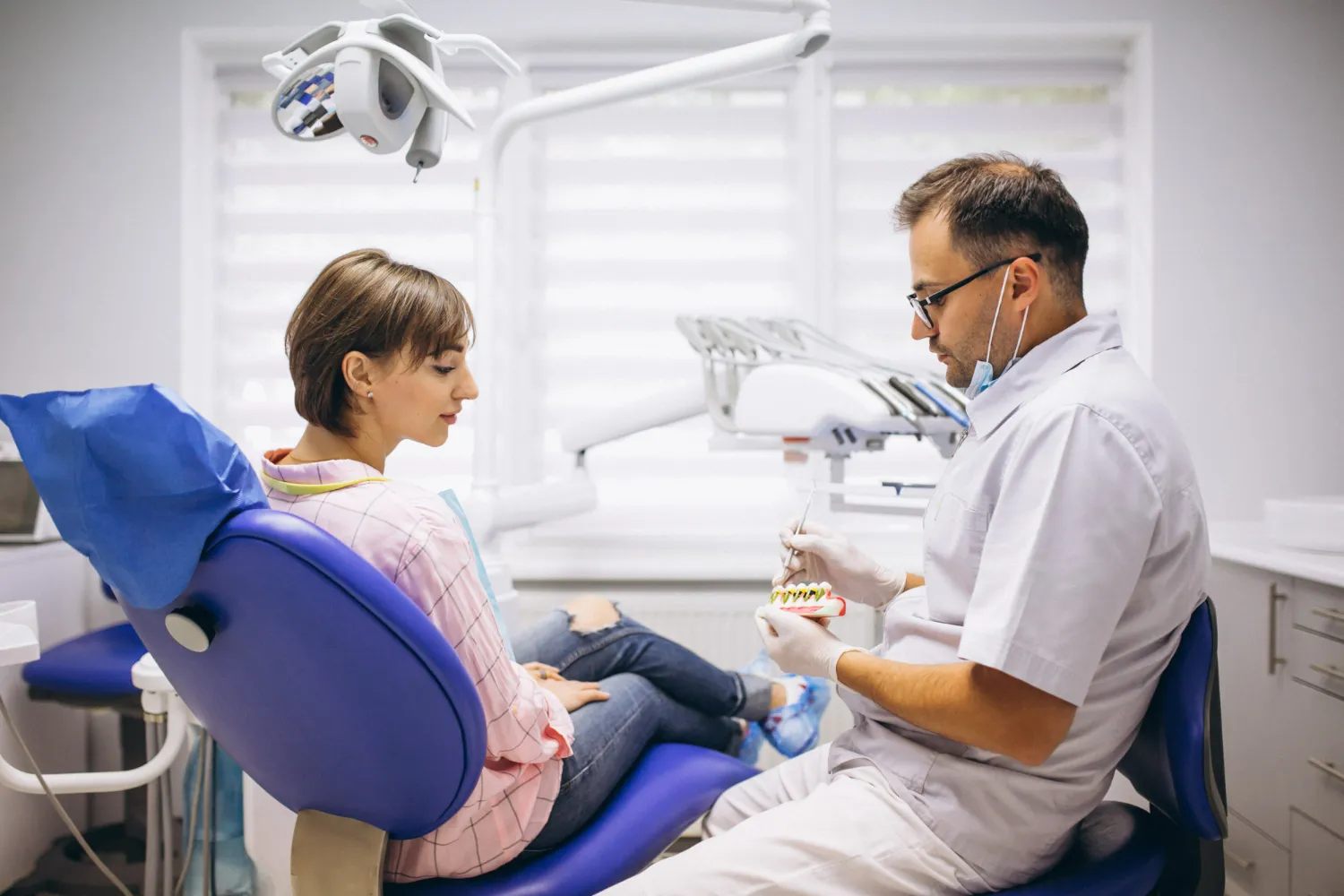 Dentist explaining dental bridge vs dental implant options to a patient using tooth models during a consultation.