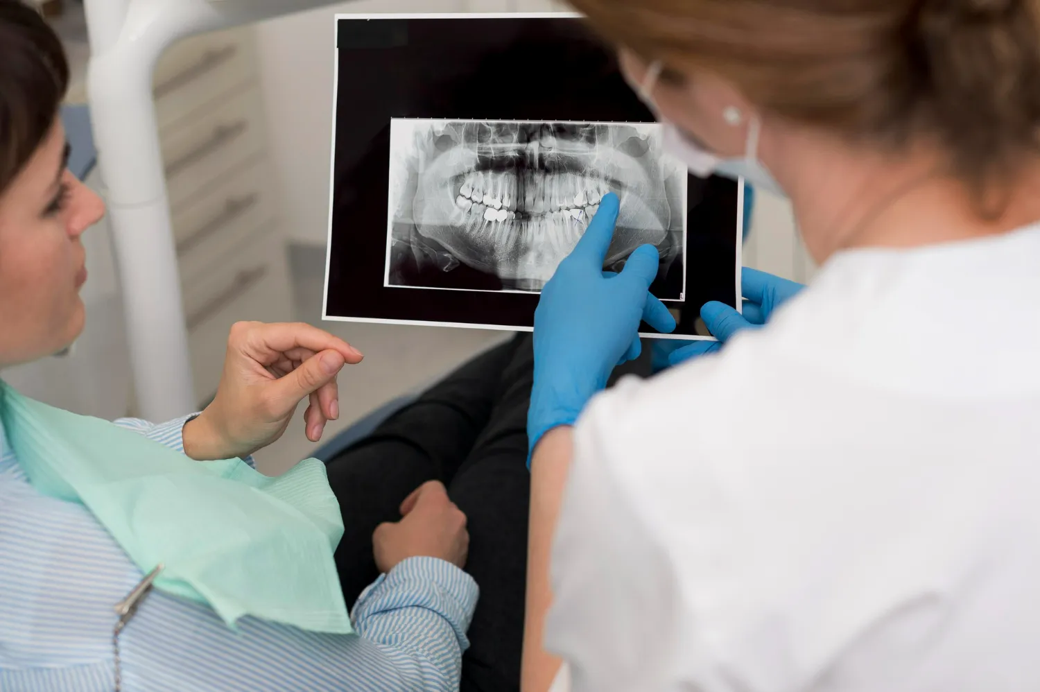 Dentist reviewing jaw X-ray while explaining teeth shaving for orthodontic planning.