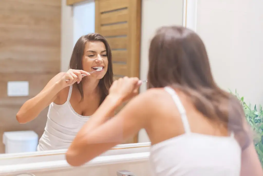 Woman brushing her teeth in bathroom as part of daily routine to keep her whitening results bright.