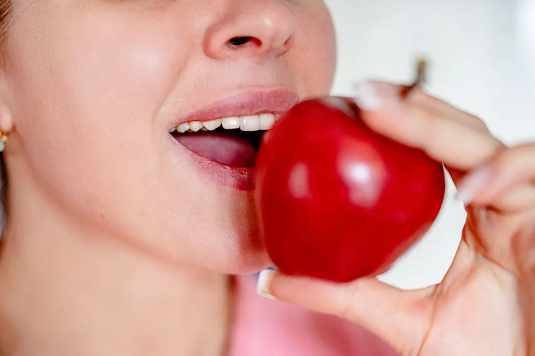 Person holding a red apple near their mouth to represent foods that are good for your teeth.