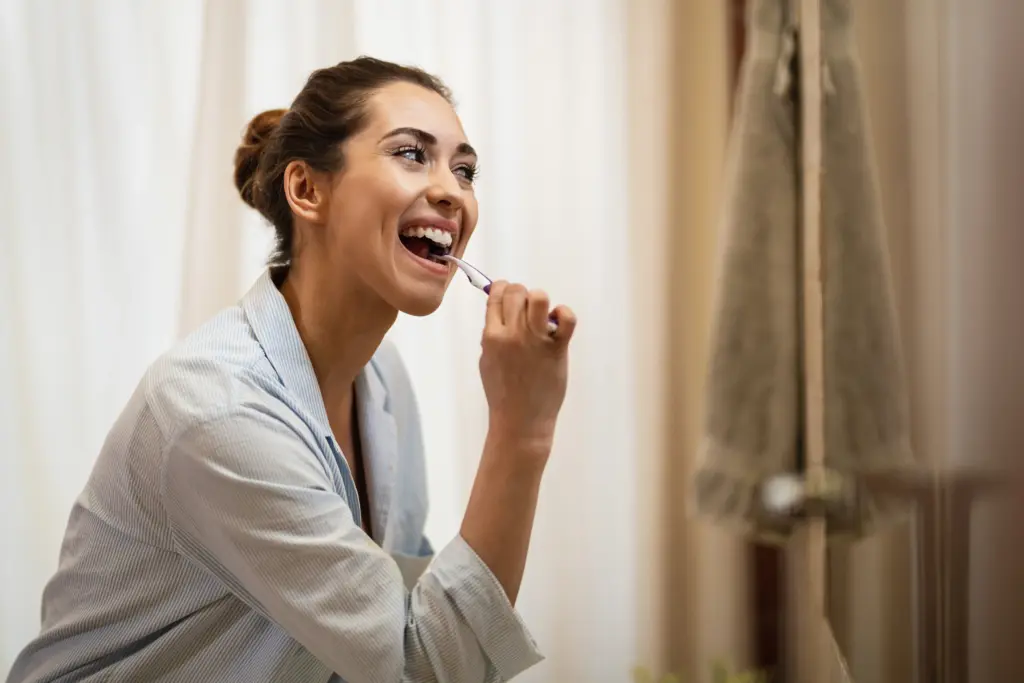 Woman brushing her teeth at home to help maintain composite bonding.