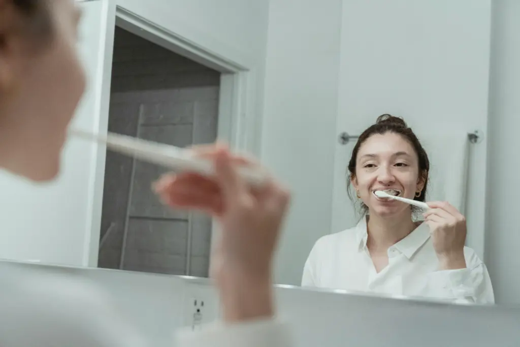 Woman brushing teeth in bathroom mirror after whitening.